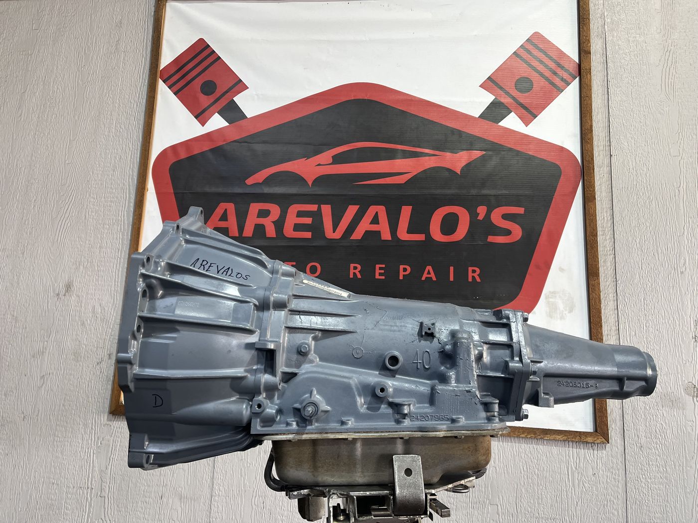 Freshly rebuilt transmission on a stand in front of the Arevalo's Auto Repair banner